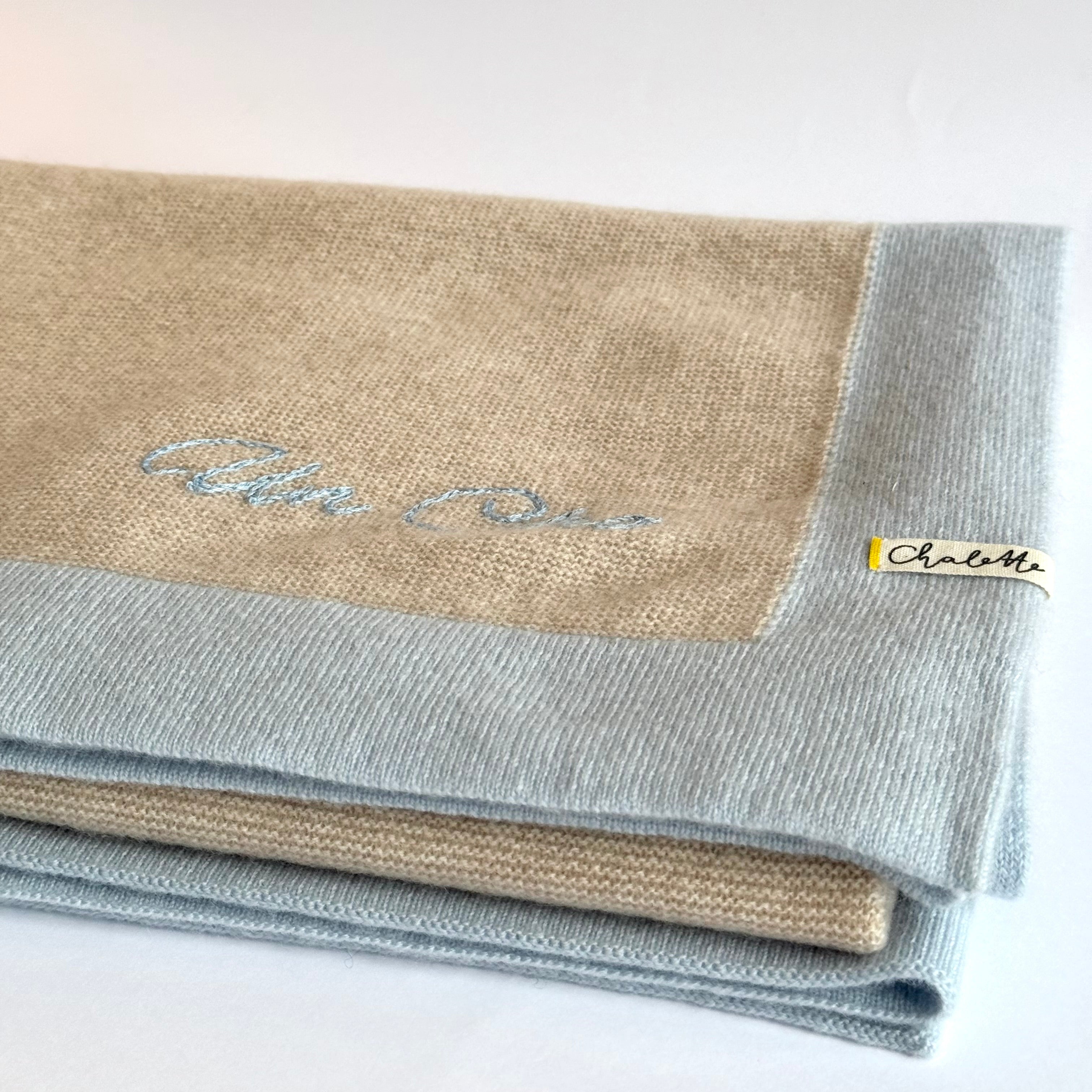 Kaschmirdecke in Beige mit Hellblauem Rand. Bestickt mit Namen "Un Cho" in Handstickerei in Blau.