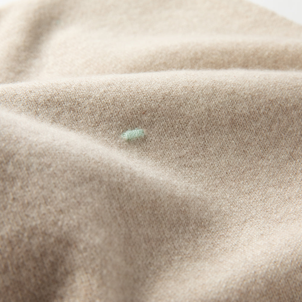 Detailaufnahme einer Babydecke in beige mit türkisfarbenen Punkten, weich drapiert mit sichtbarer Struktur