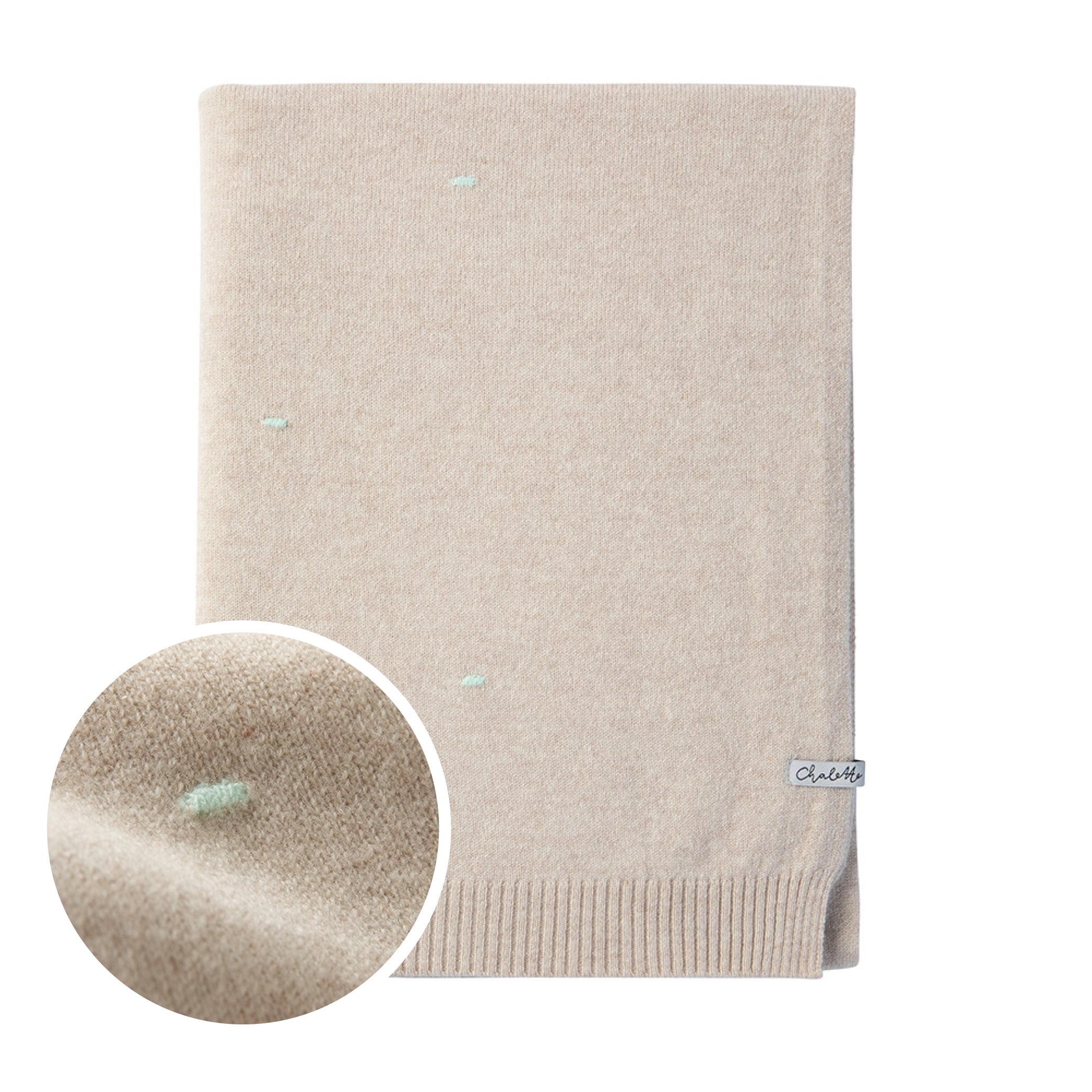 Gefaltete Kaschmirdecke in beige mit türkisfarbenen Punkten auf weißem Hintergrund, links im Bild eine Nahaufnahme des Strickmusters der Decke