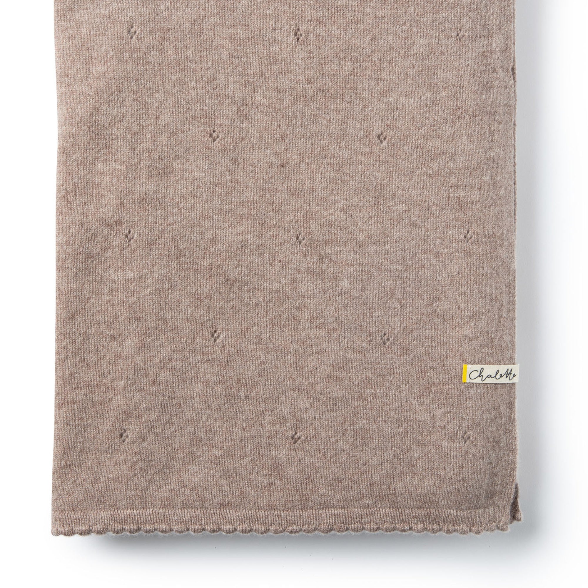 Nahaufnahme einer Kaschmirdecke in beige mit Lochmuster, gefaltet auf weißem Hintergrund