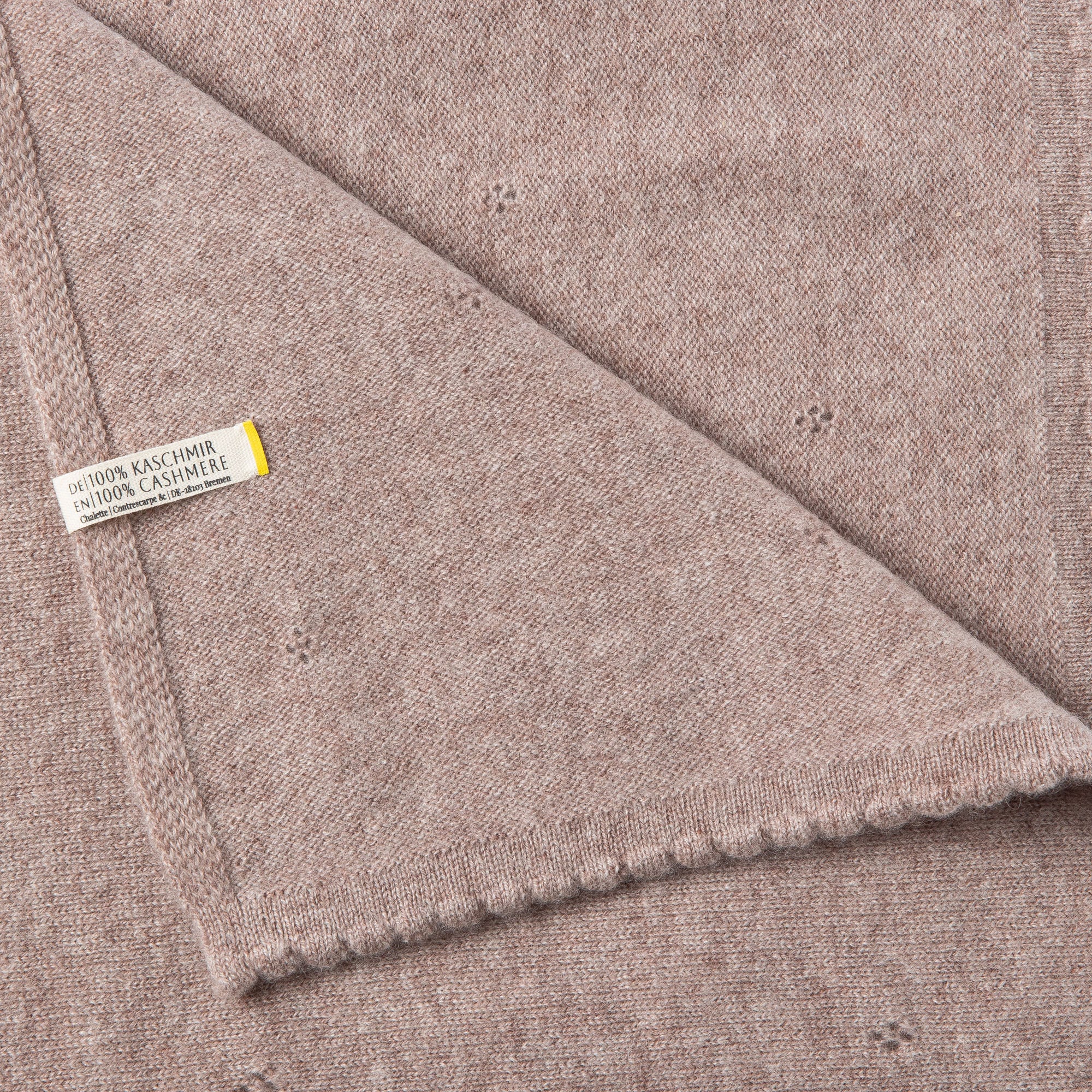 Detailaufnahme einer beigen Kaschmirdecke mit sichtbarem Etikett: 100% Kaschmir