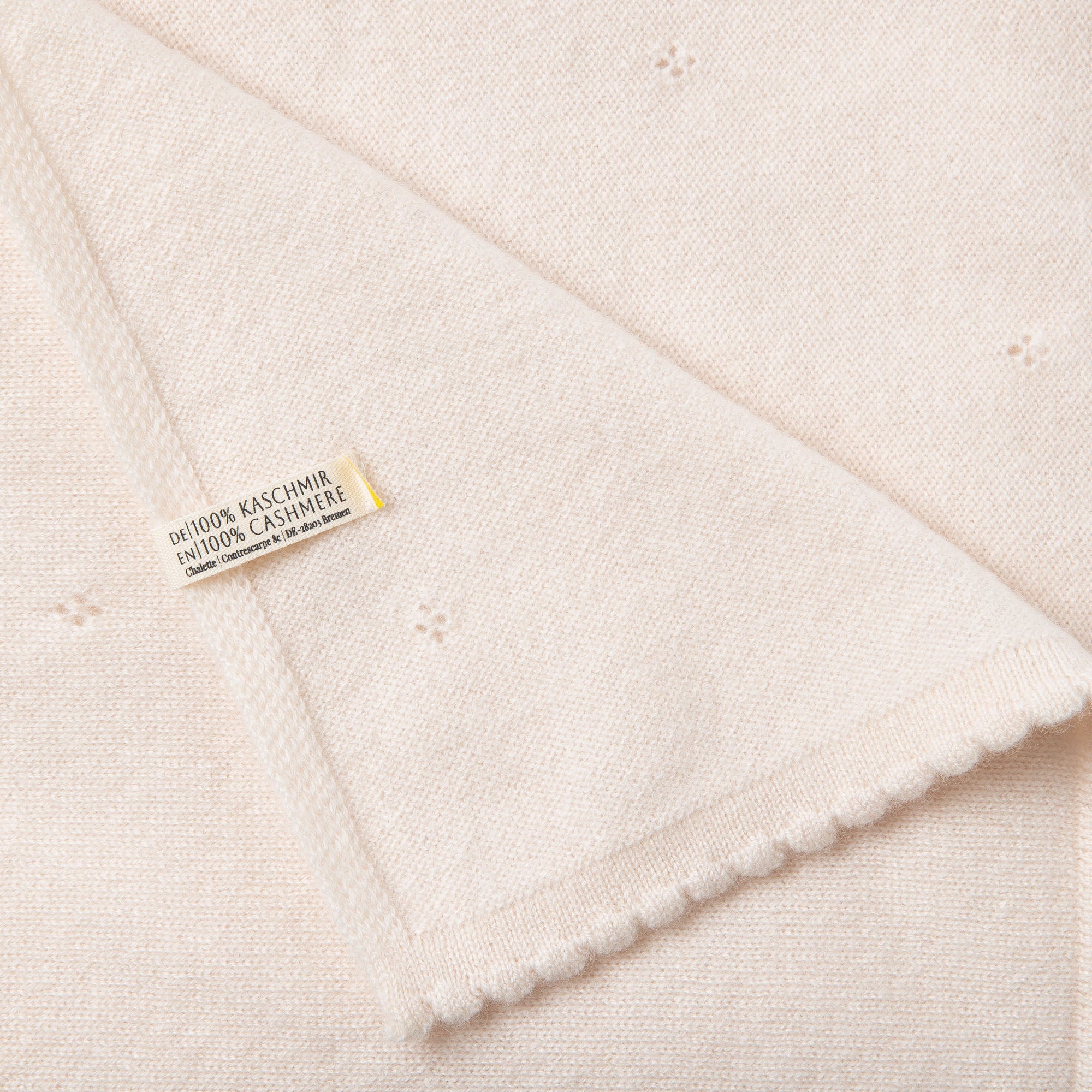 Detailaufnahme einer Kaschmirdecke in off-white mit Lochmuster mit sichtbarem Etikett: 100% Kaschmir