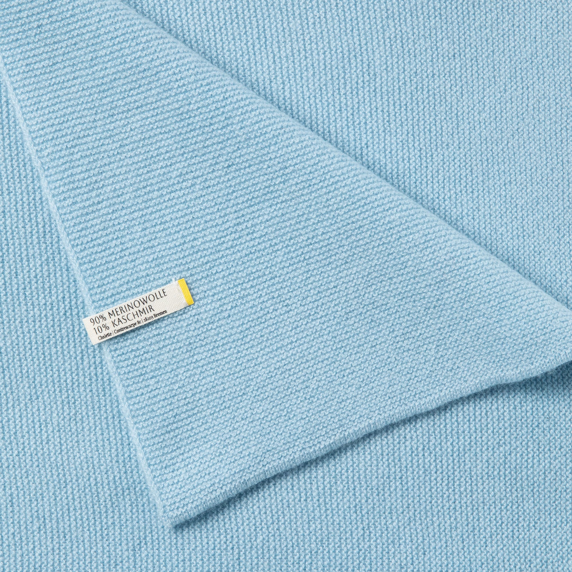 Detailaufnahme einer blauen Babydecke mit sichtbarem Etikett: 90% Merinowolle, 10% Kaschmir