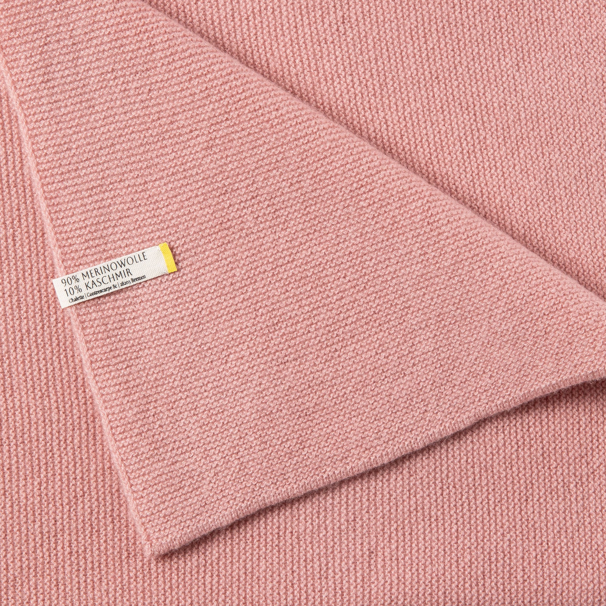 Detailaufnahme einer Babydecke in rosa mit sichtbarem Etikett: 90% Merinowolle, 10% Kaschmir