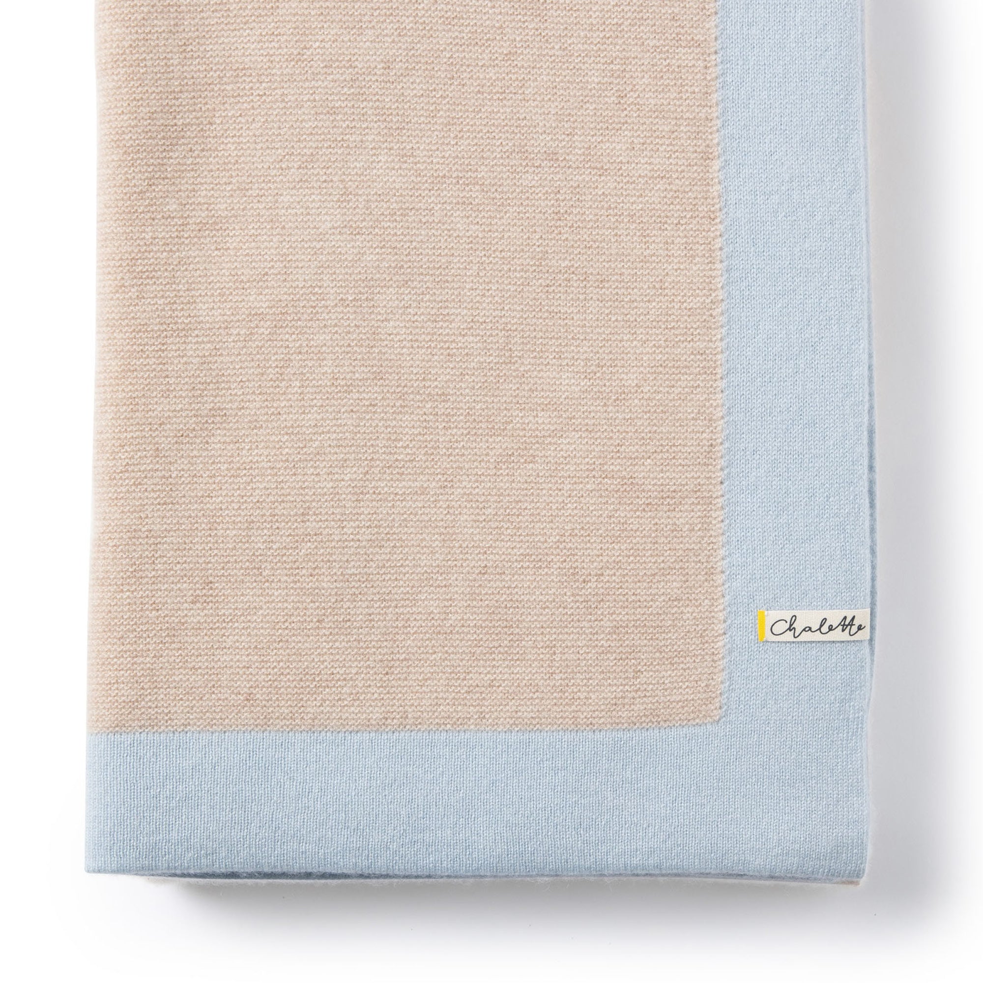 Gefaltete Babydecke in beige mit blauem Rand auf weißem Hintergrund