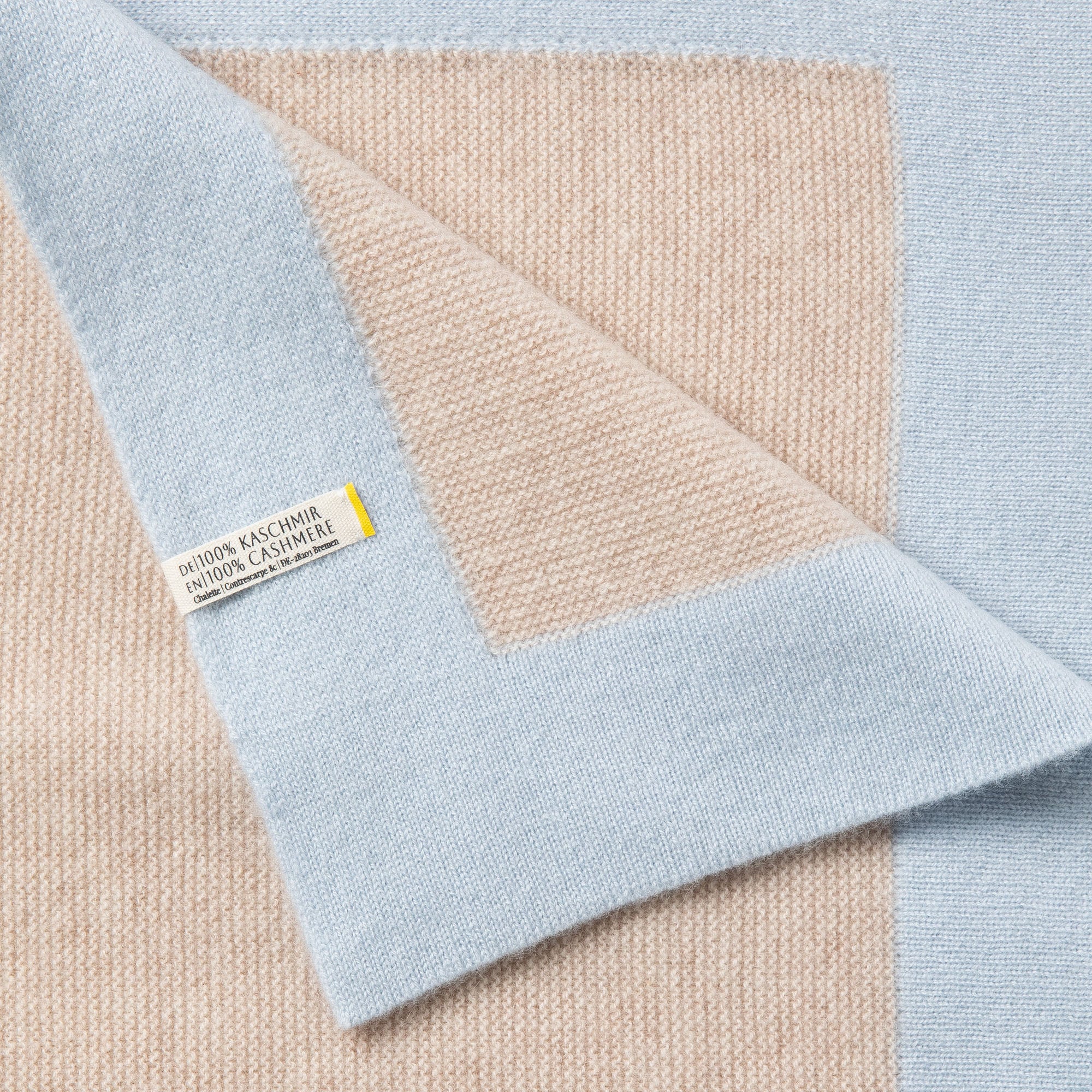 Detailaufnahme einer Babydecke in beige mit blauem Rand mit sichtbarem Etikett: 100% Kaschmir