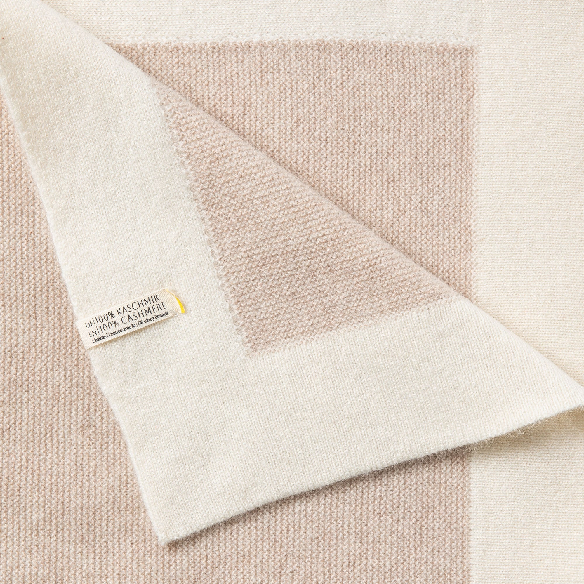 Detailaufnahme einer Babydecke aus Kaschmir in beige mit Rand in off-white mit feinem Strickmuster, sichtbares Etikett: 100% Kaschmir