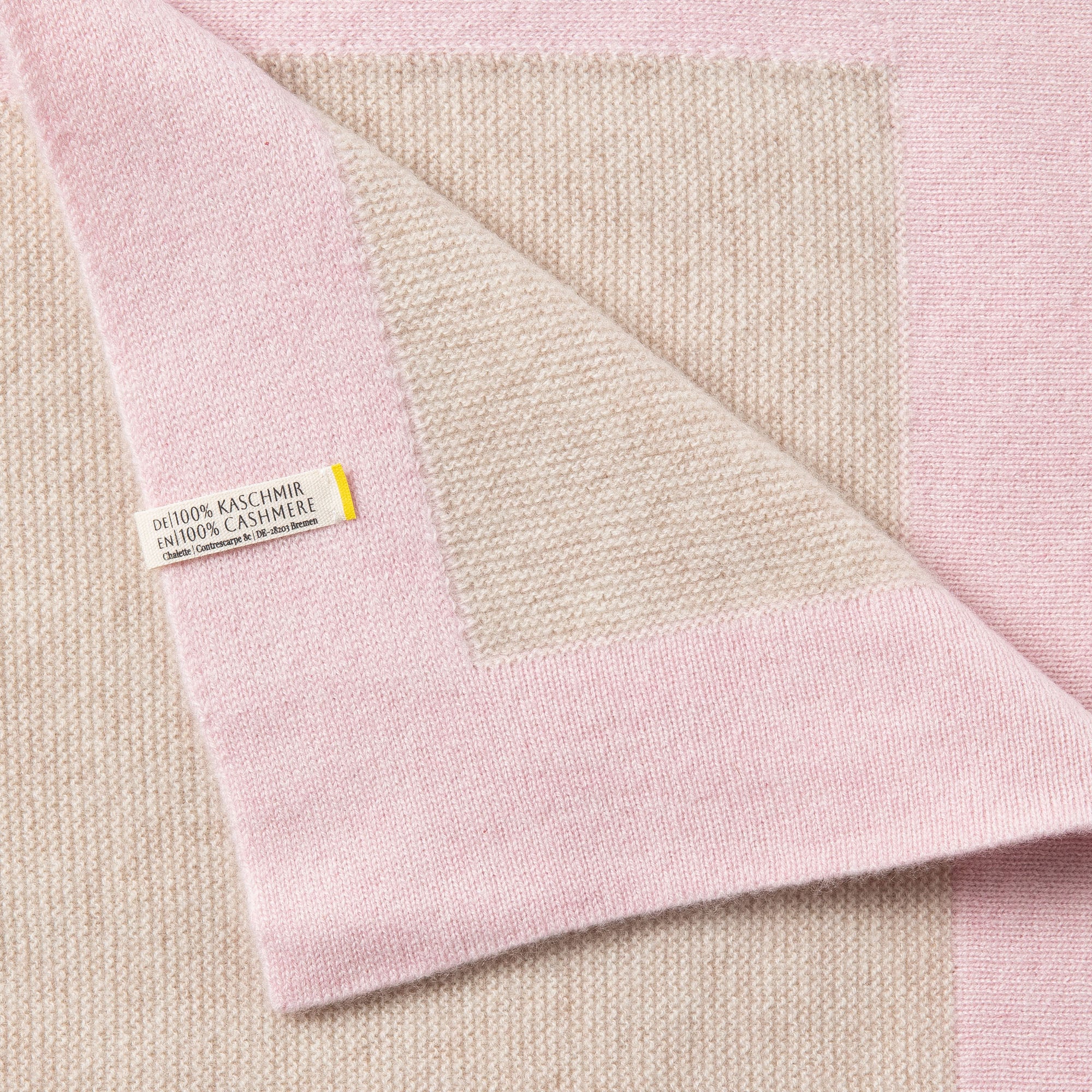 Detailaufnahme einer Babydecke in beige mit rosa Rand mit sichtbarem Etikett: 100% Kaschmir