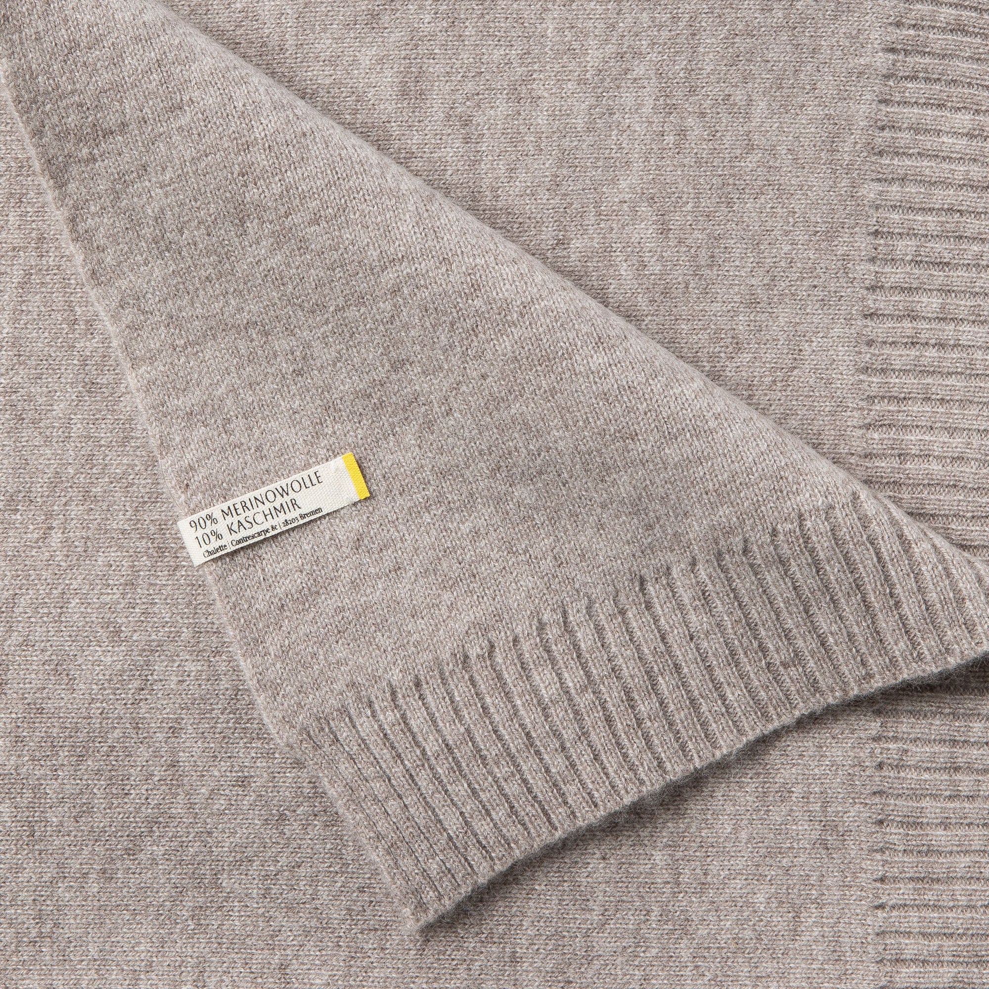 Detailaufnahme einer grauen Sofadecke mit sichtbaren Etikett: 90% Merinowolle, 10% Kaschmir