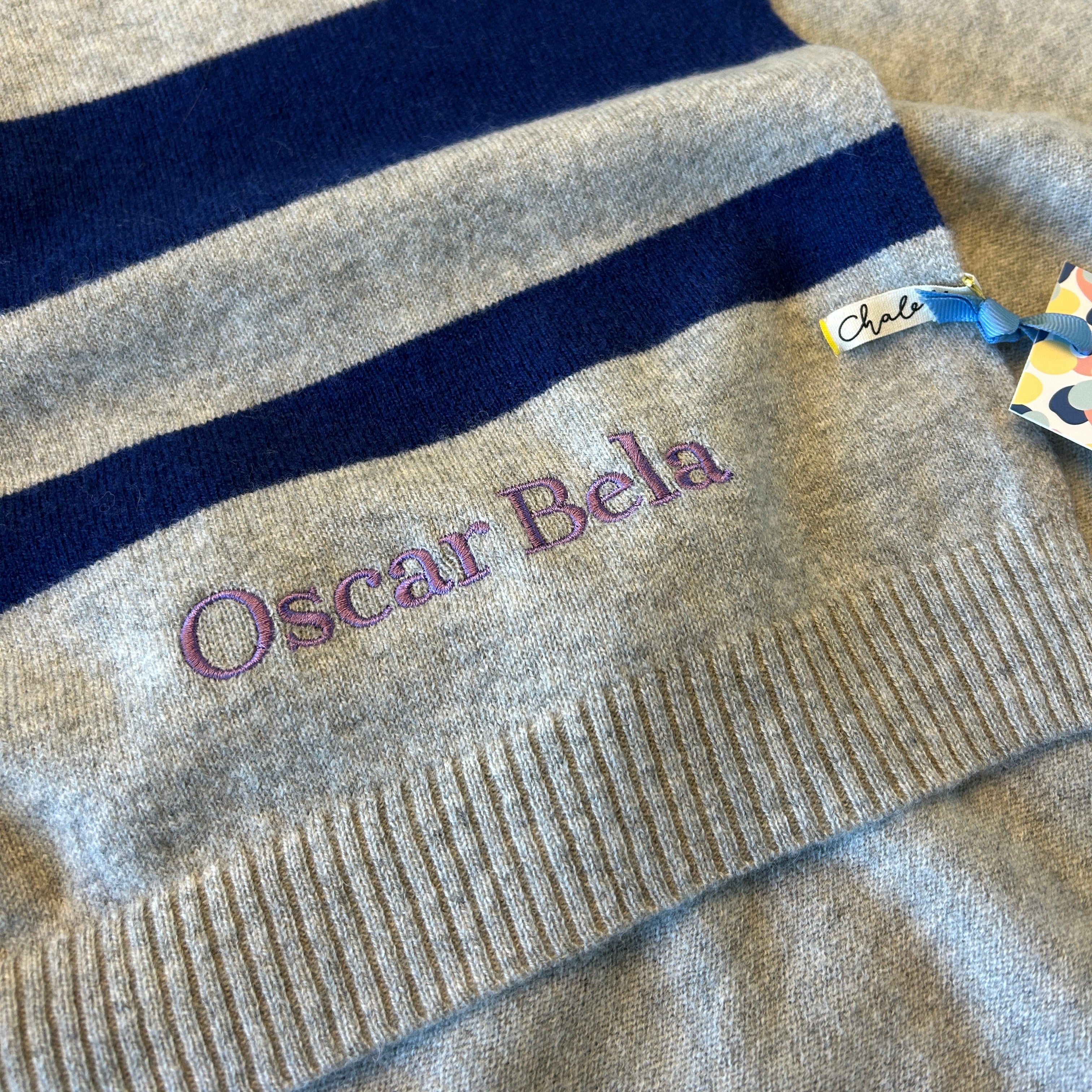 Babydecke in Grau mit Blauen Streifen. Bestickt mit Namen "Oscar Bela" in Lila.