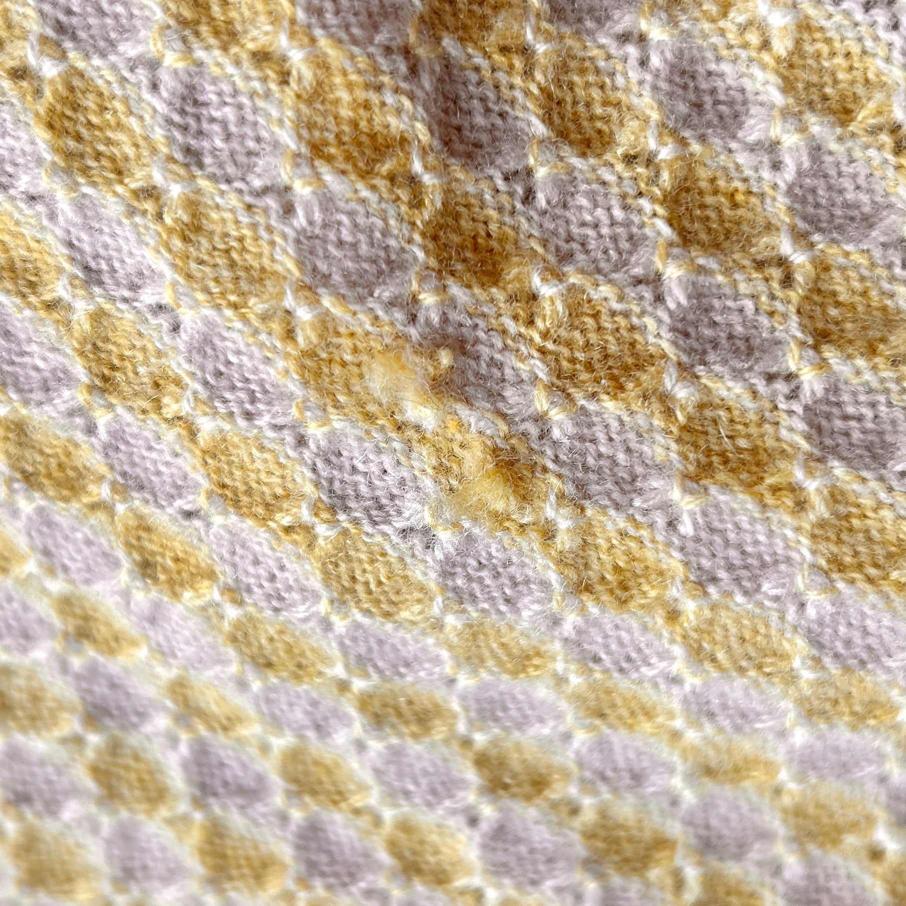 Detailaufnahme einer Babydecke in Beige und Gelb. Die Decke hat ein kleines Loch.