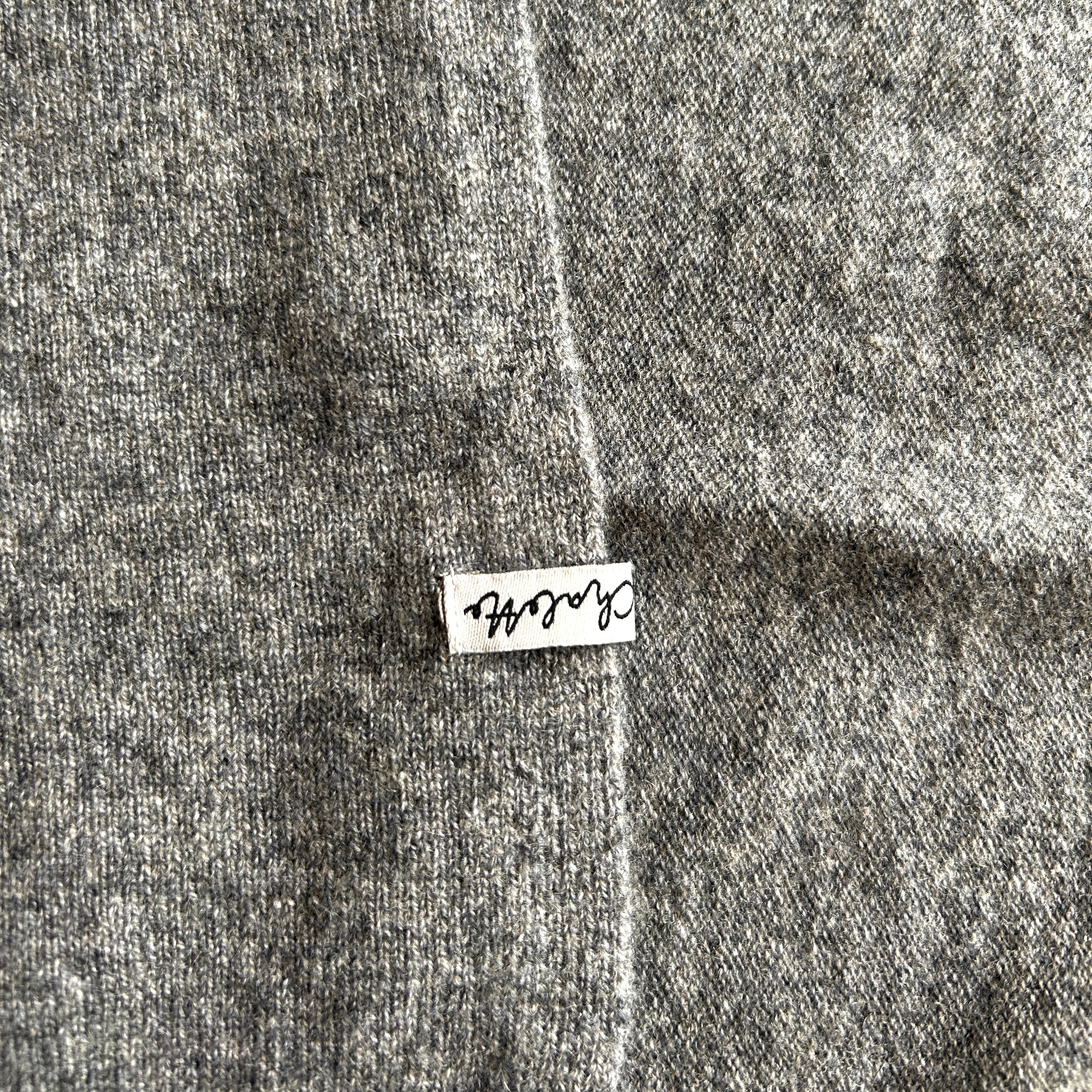 Nahaufnahme einer Kaschmirdecke in Grau. Das Etikett ist falsch aufgenäht.