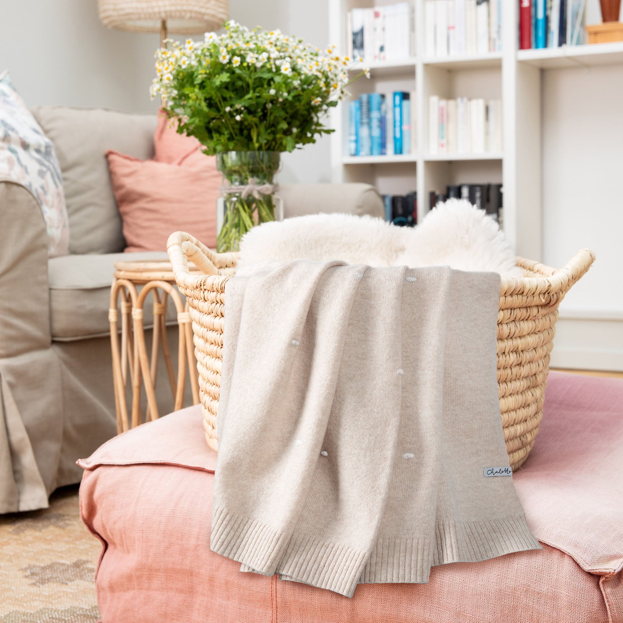 Kaschmirdecke in beige mit weißen Punkten über einem Korb mit Lammfell, auf rosafarbenem Pouf im Wohnzimmer drapiert