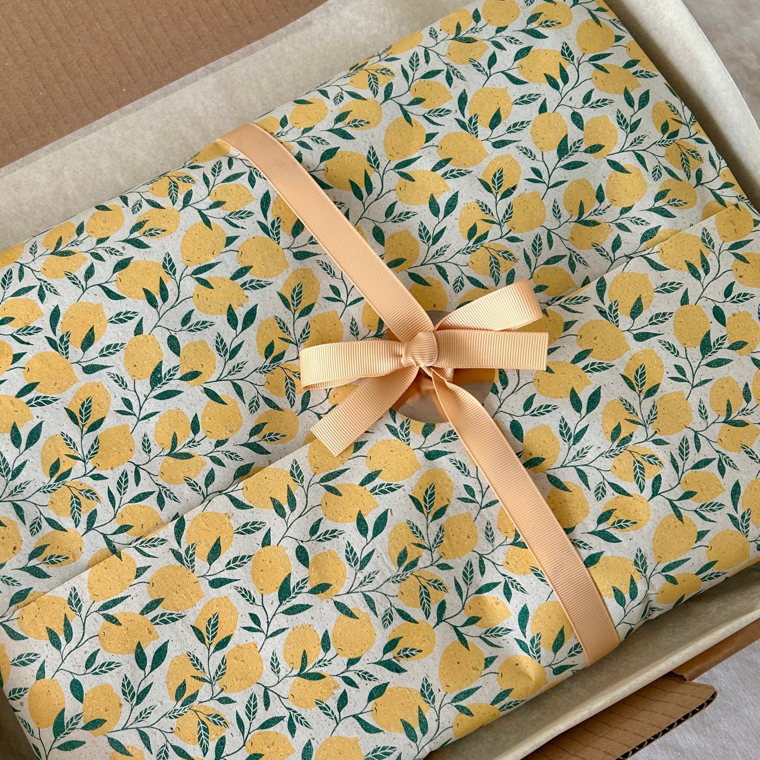 Geschenkverpackung mit Zitronenmusterpapier und beigefarbener Schleife, in offenem Versandkarton liegend