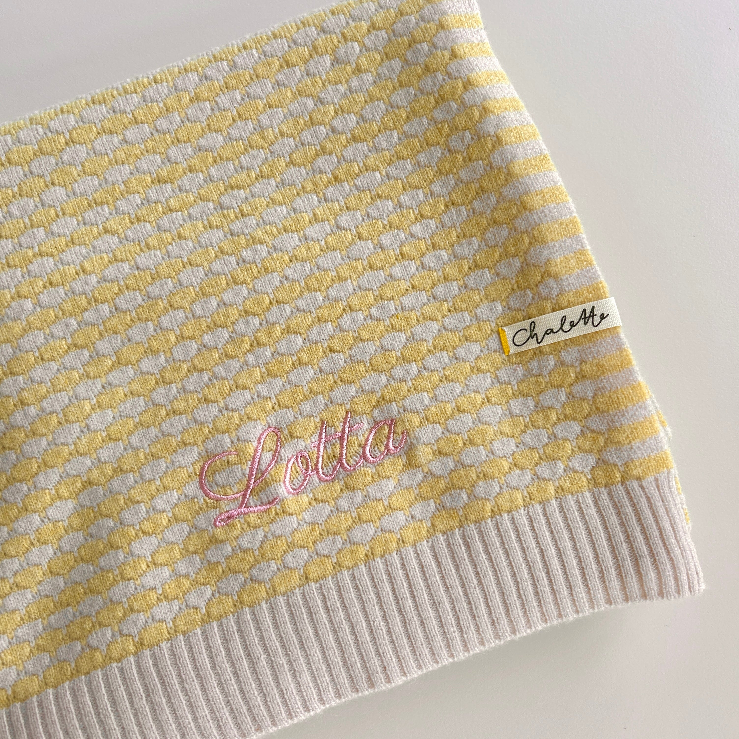 Zusammengelegte Kaschmirdecke in beige und gelb personalisiert mit gesticktem Namen „Lotta“ in rosa