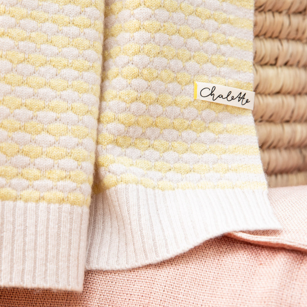Babydecke mit strukturiertem Wabenmuster in Gelb und Beige, drapiert über einen Korb, mit sichtbarem Etikett: Chalette