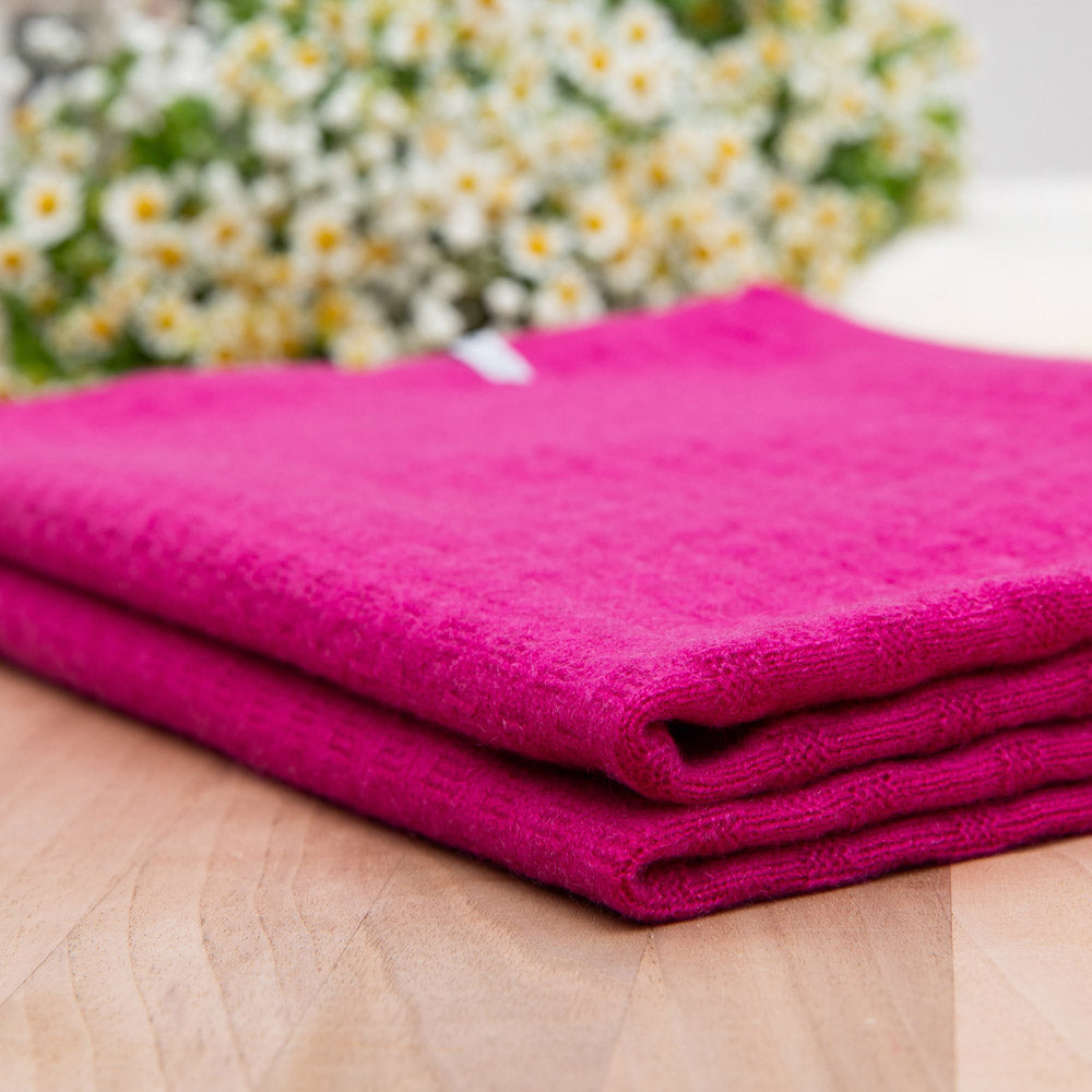 Gefaltete Kaschmirdecke in Pink mit Waffelmuster auf Holztisch, Hintergrund mit Blumen