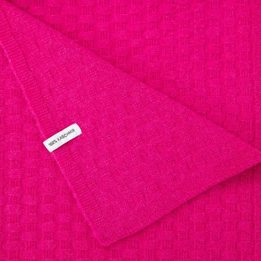 Detailaufnahme einer Kaschmirdecke in Pink mit Waffelmuster, mit sichtbarem Etikett: 100% Kaschmir