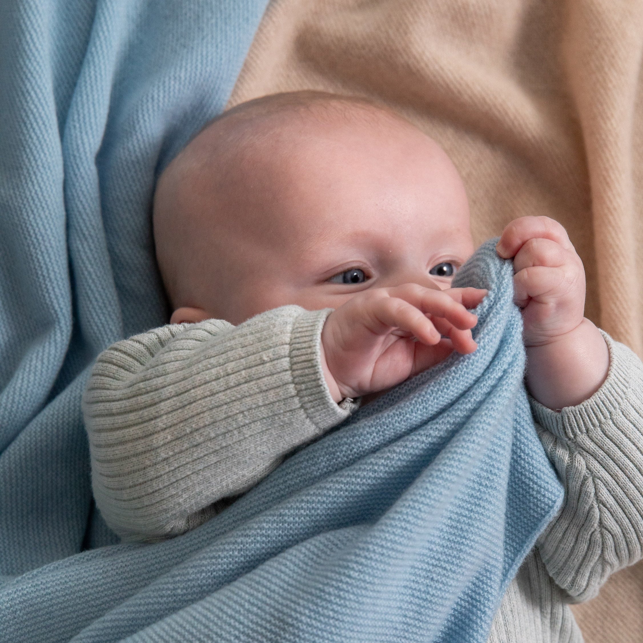 Baby mit hellblauer Kaschmir Light Babydecke von Chalette, auf beigefarbender Decke liegend
