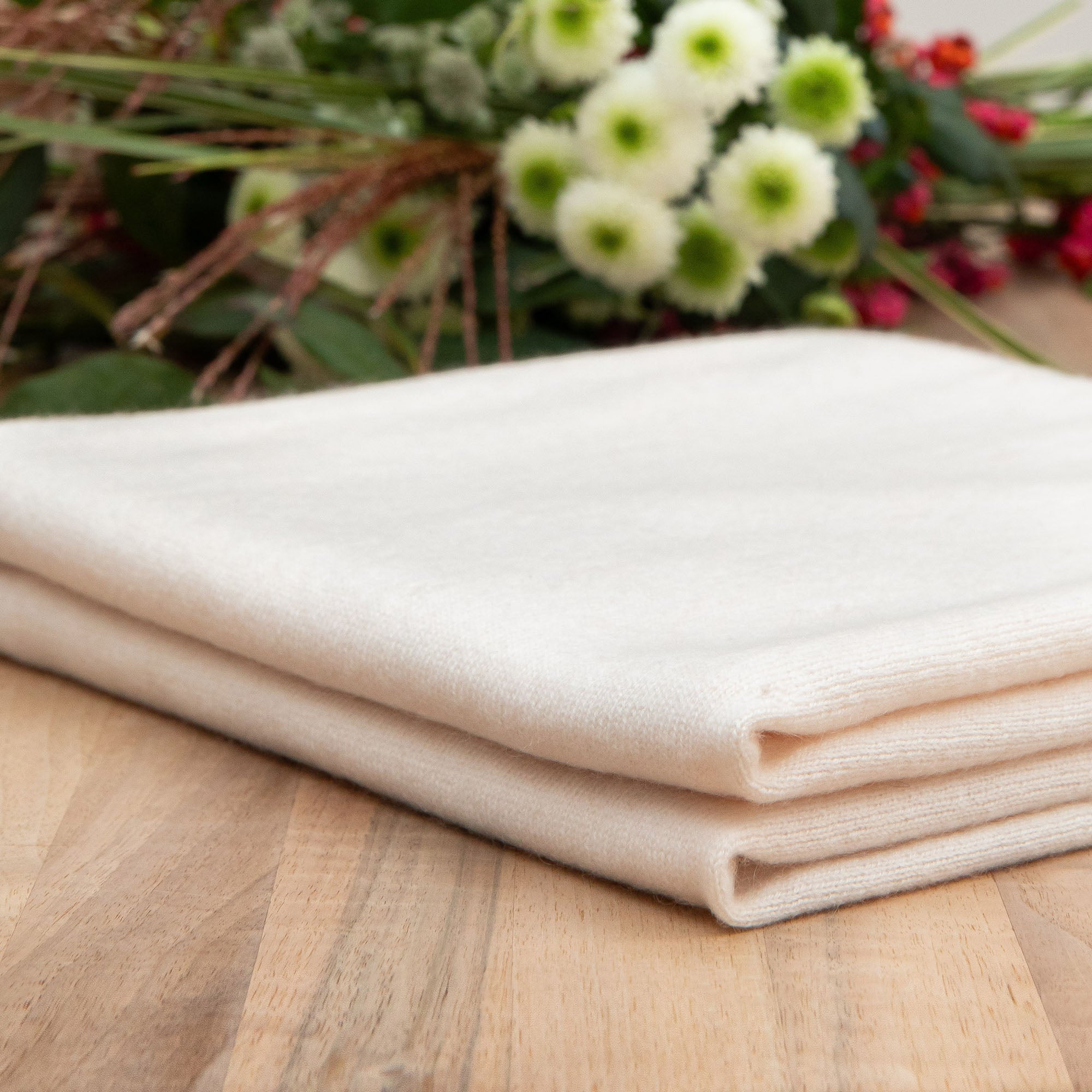 Gefaltete Kaschmirdecke in off-white auf Tisch, Hintergrund mit Blumen