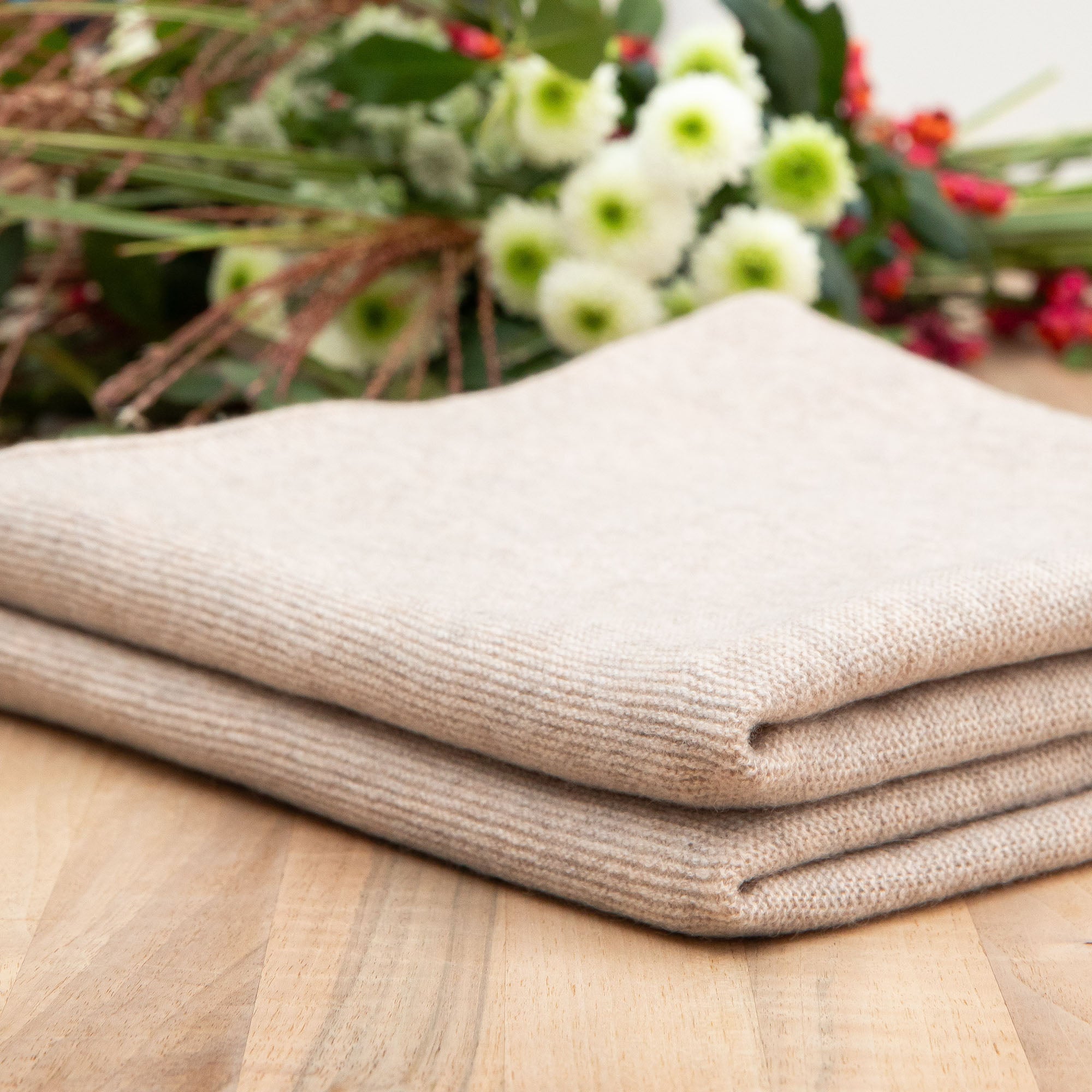 Gefaltete Babydecke in beige auf Holztisch, Hintergrund mit Blumen