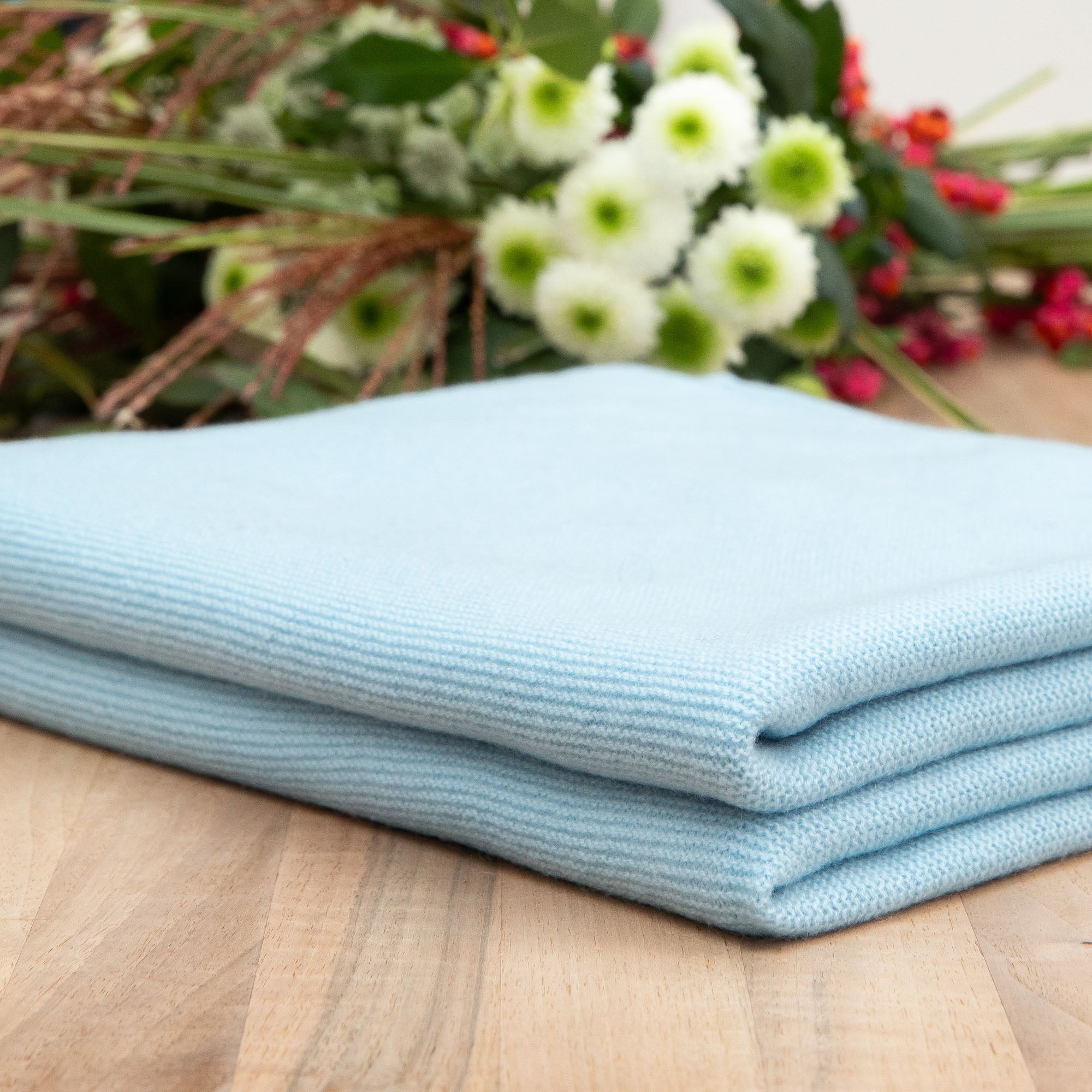 Gefaltete Babydecke in blau auf Holztisch, Hintergrund mit Blumen