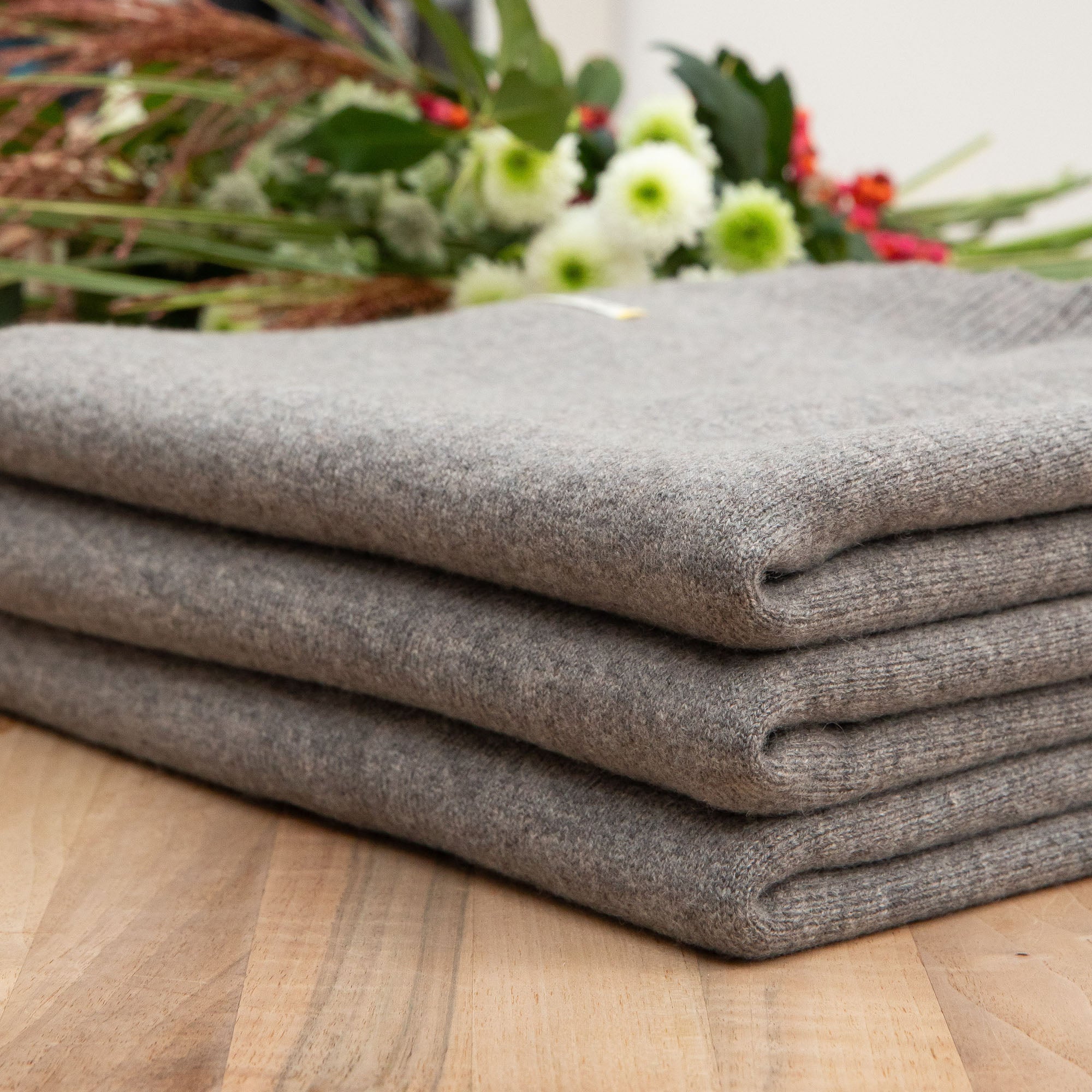 Gefaltete Sofadecke von Chalette auf Holztisch, Hintergrund mit Blumen