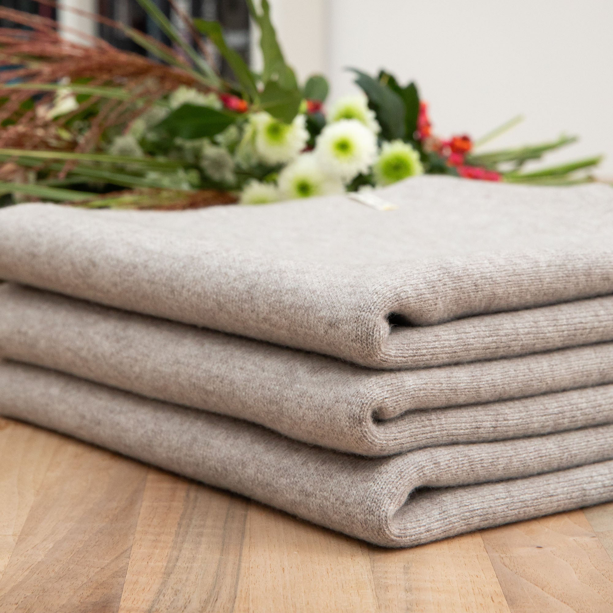 Nahaufnahme einer gefalteten Sofadecke in grau auf einem Holztisch, Hintergrund mit Blumen