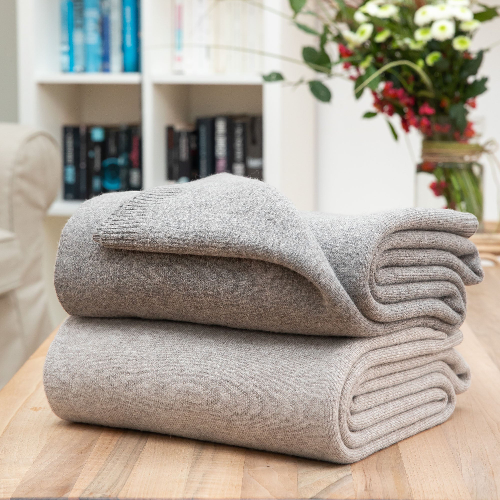 Gefaltete Sofadecken in grau und dunkelgrau auf Tisch, Hintergrund mit Sofa und Blumen