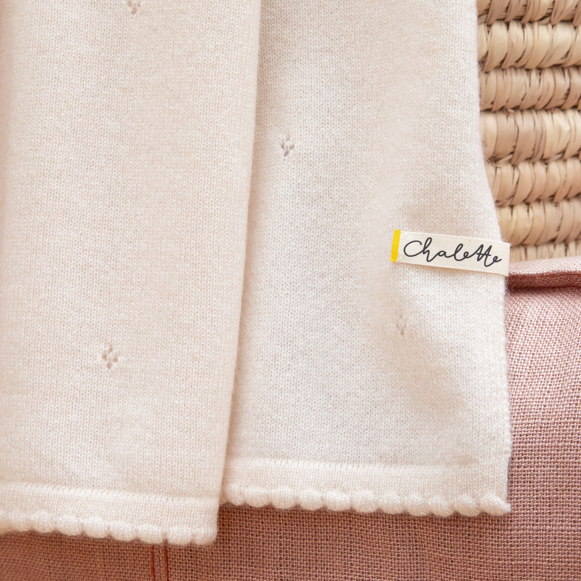 Detailaufnahme einer Babydecke aus Kaschmir in off-white mit Lochmuster mit sichtbarem Etikett: Chalette