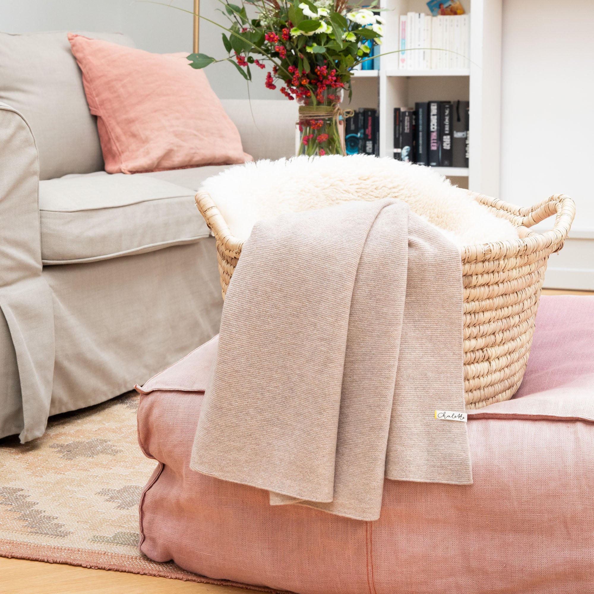 Babydecke in beige über einem Korb mit Lammfell auf rosafarbenem Pouf im Wohnzimmer drapiert