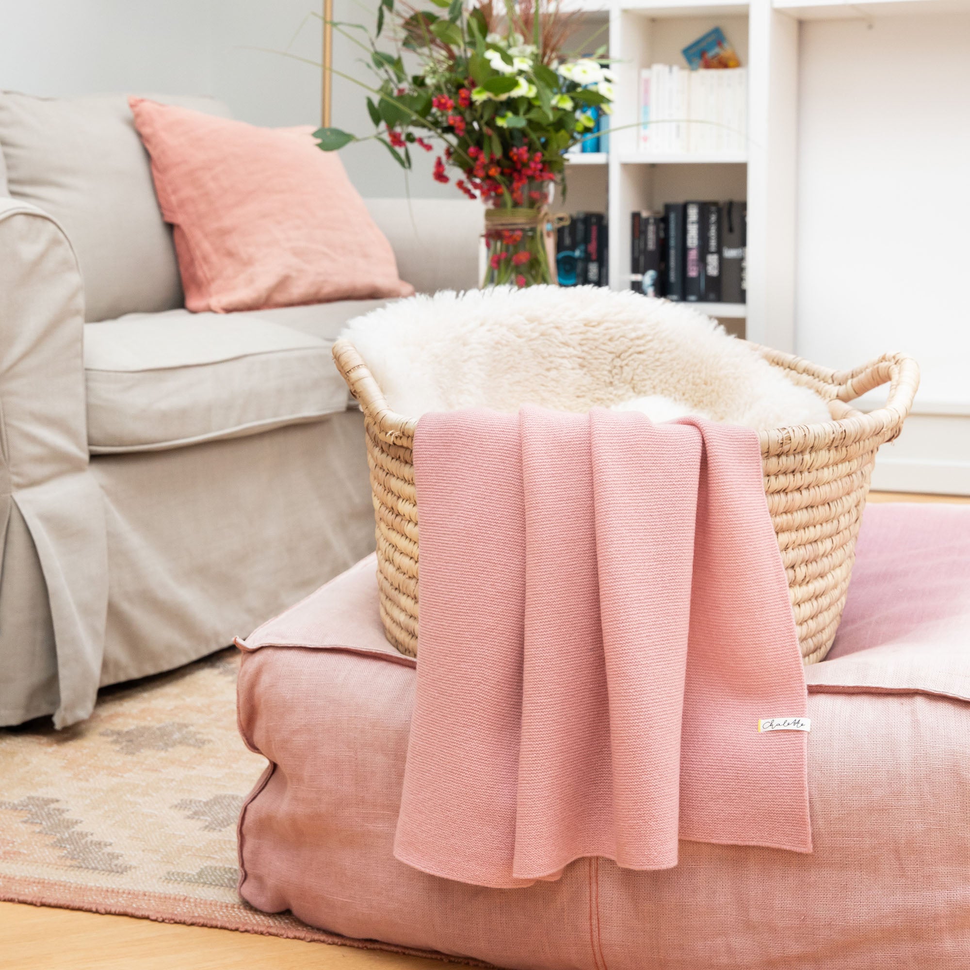 Babydecke aus Kaschmir und Merinowolle in rosa über einem Korb mit Lammfell, auf rosafarbenem Pouf im Wohnzimmer drapiert