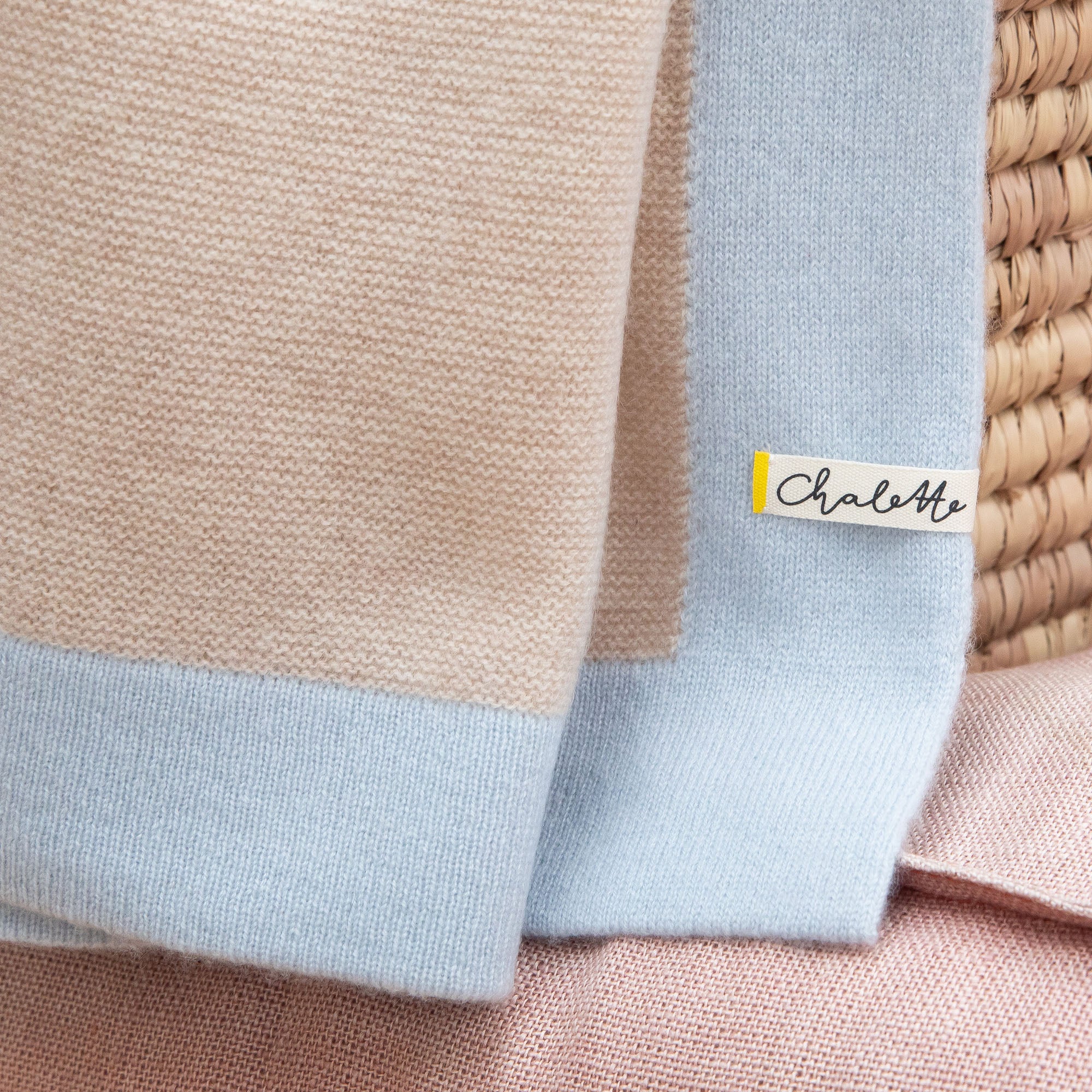 Nahaufnahme einer Babydecke aus Kaschmir in beige mit blauem Rand mit sichtbarem Etikett: Chalette