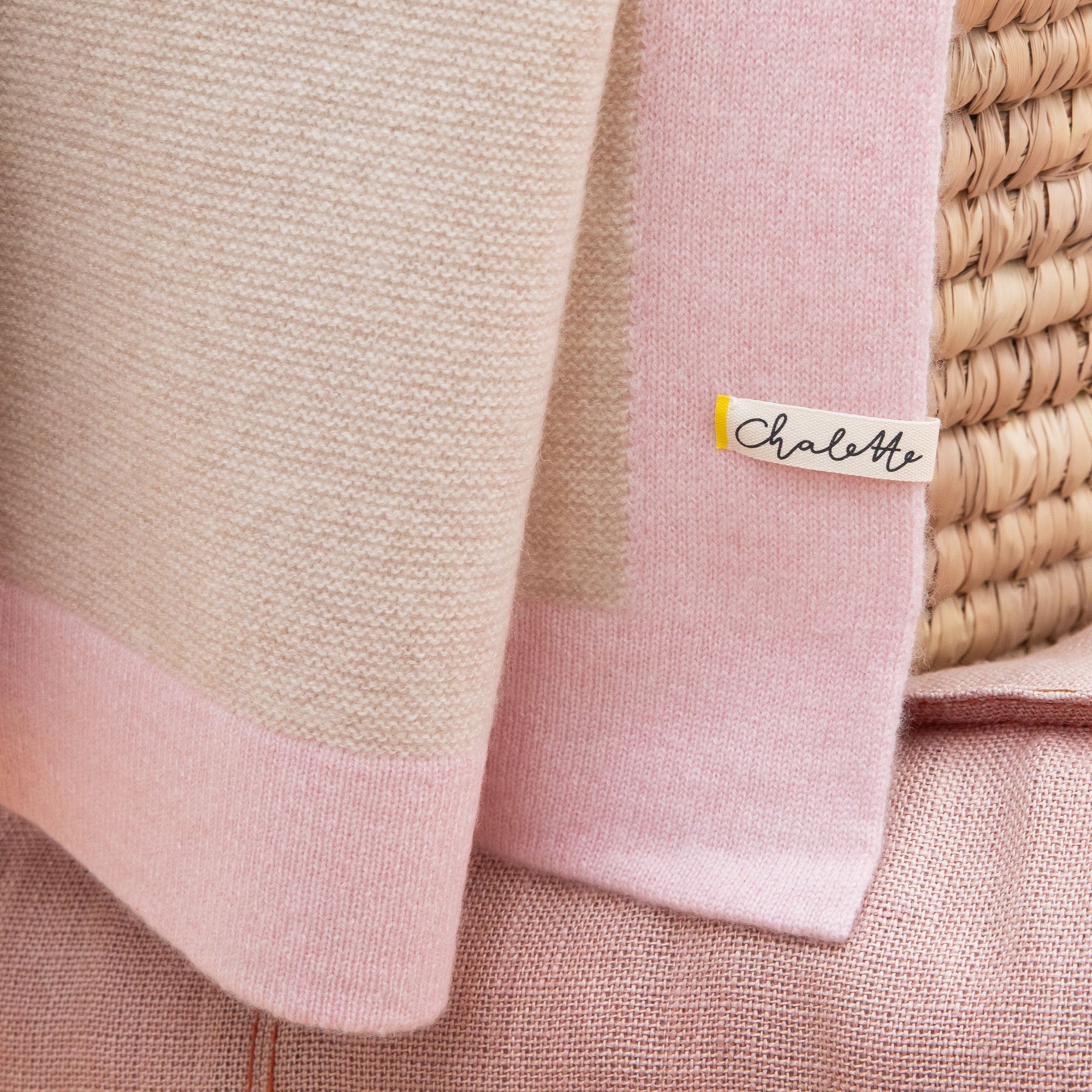 Nahaufnahme einer Kaschmirdecke in beige mit rosa Rand mit sichtbarem Etikett: Chalette