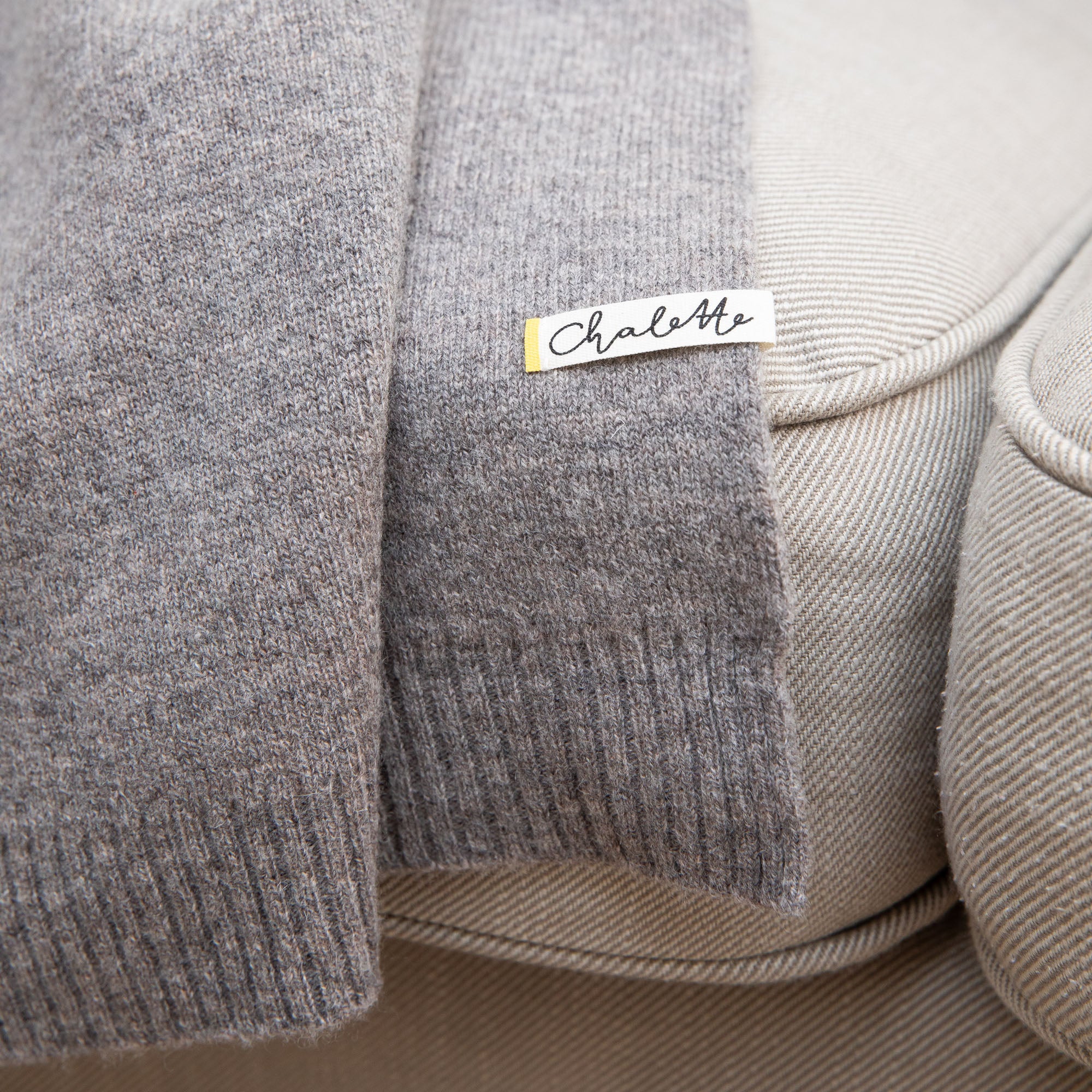 Nahaufnahme einer grauen Sofadecke von Chalette, auf einem Sofa liegend. Etikett mit Markenname
