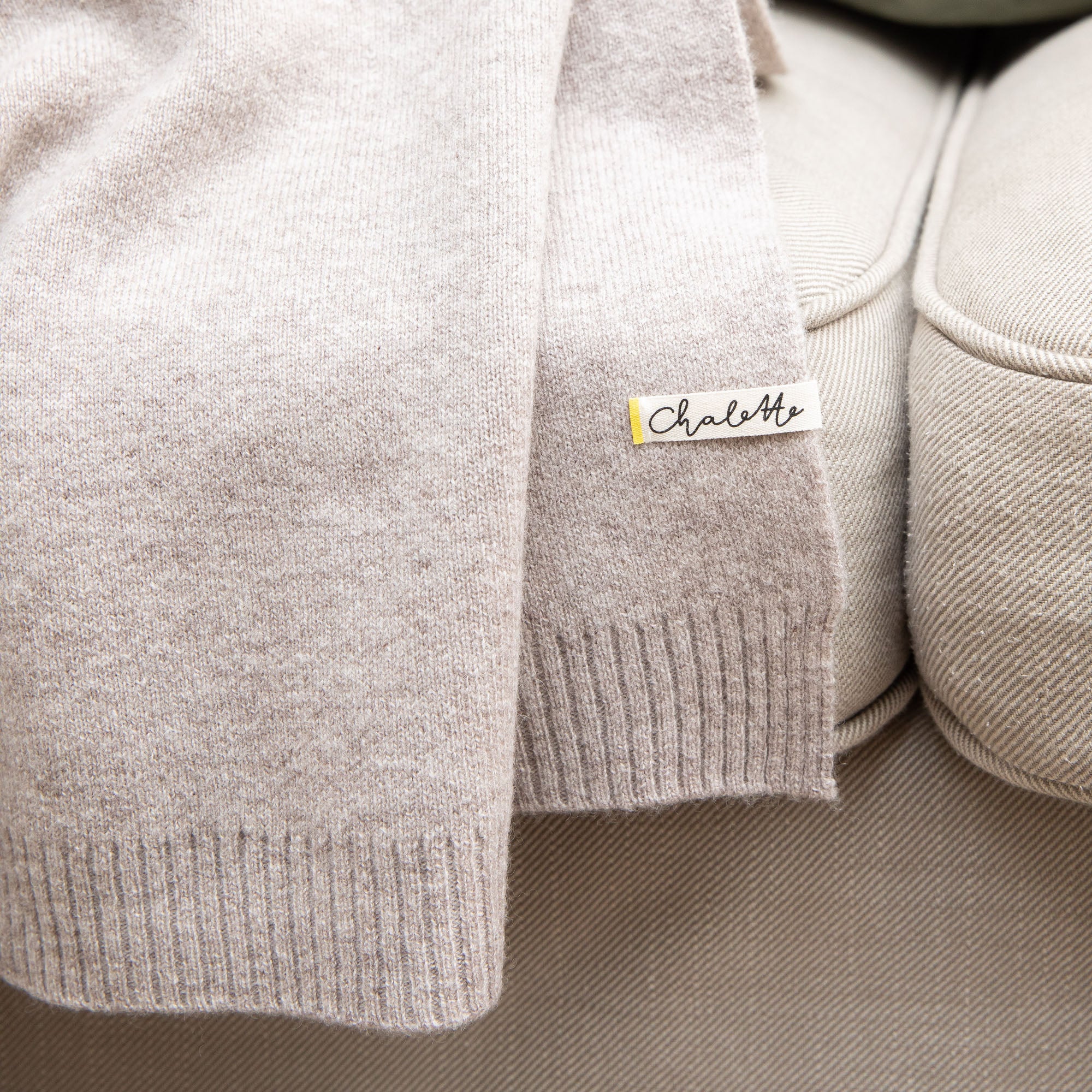 Nahaufnahme einer Sofadecke in grau, auf Sofa liegend. Etikett mit Chalette