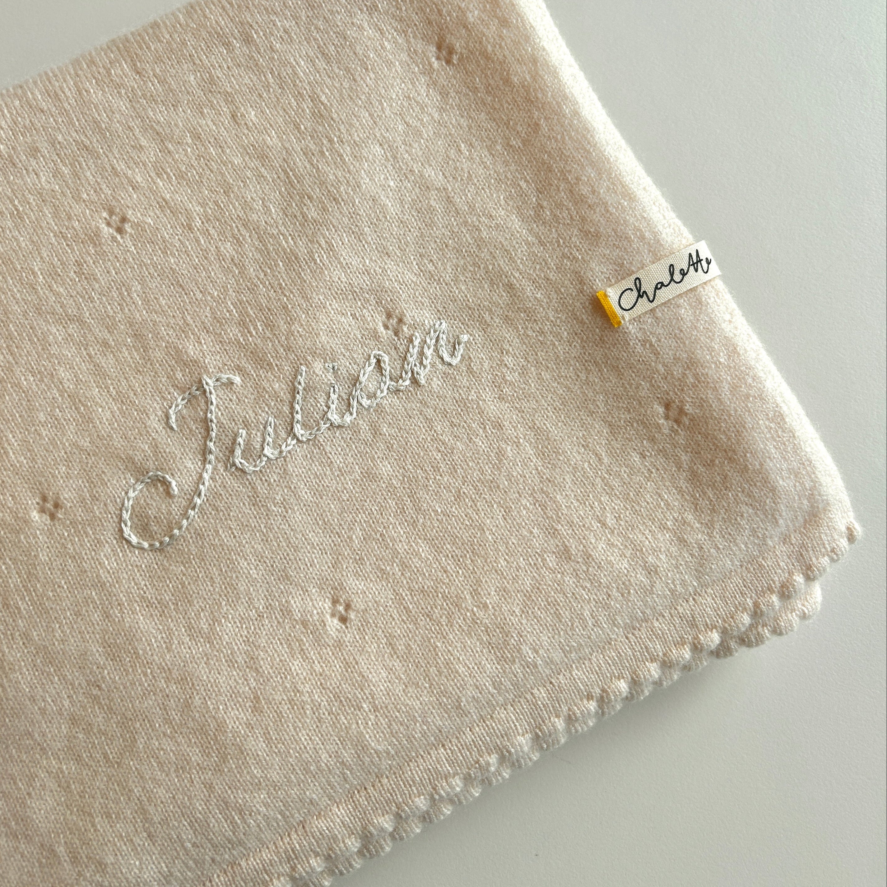Kaschmirdecke in Off-White mit Lochmuster. Bestickt mit Name "Julian" mit Handstickerei in Beige.