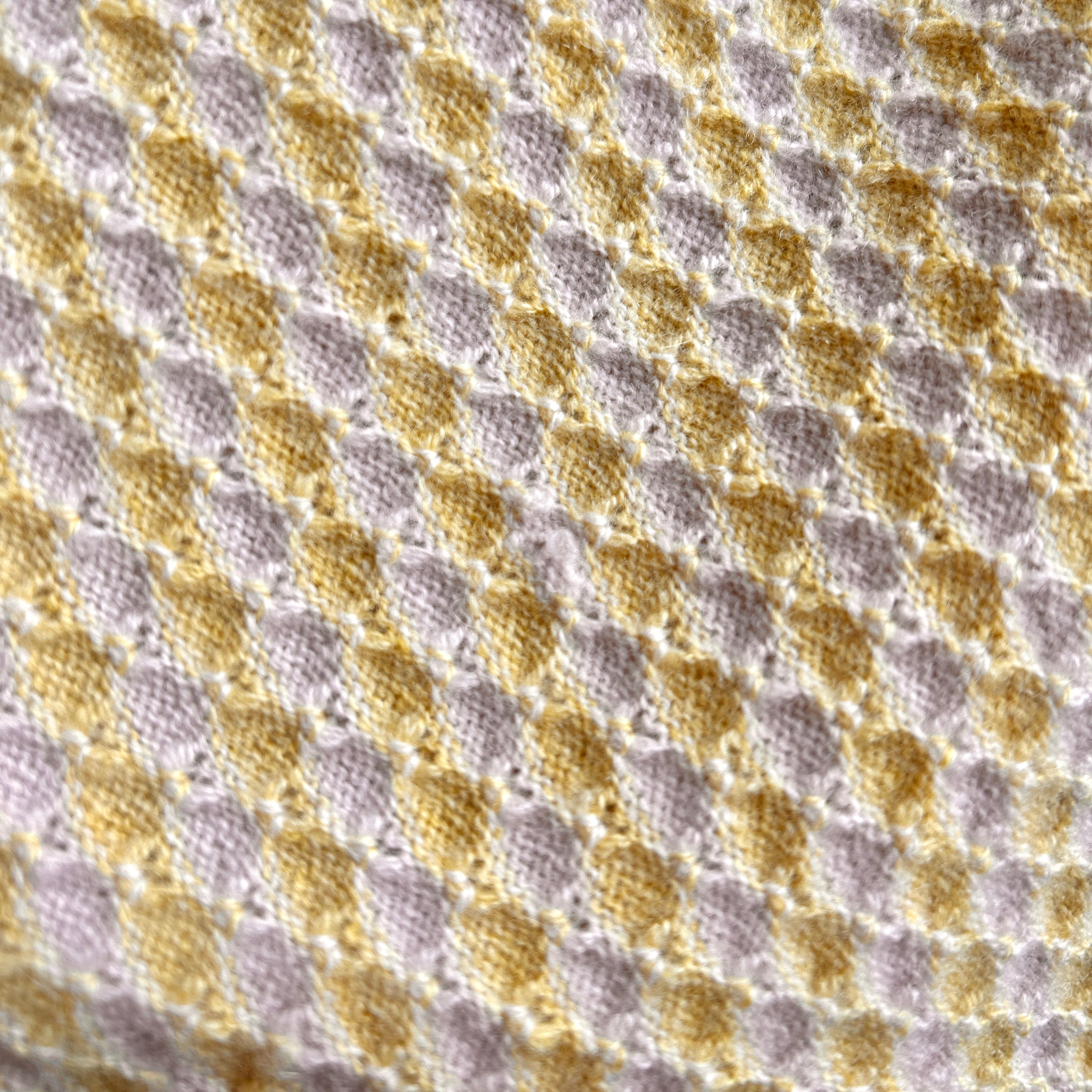 Detailaufnahme einer Babydecke in Beige und Gelb. Die Decke hat ein kleines Loch.