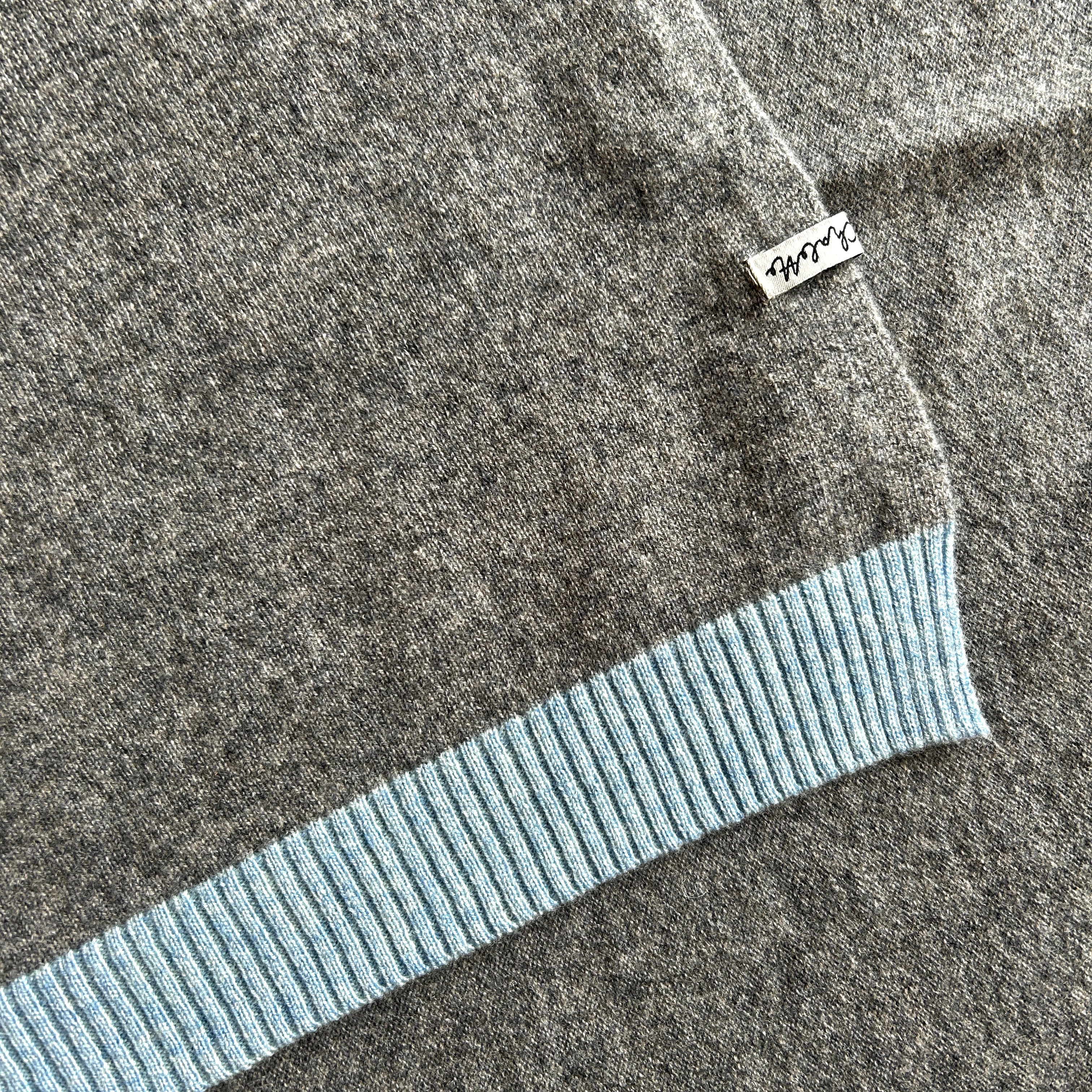 Ausschnitt einer Kaschmirdecke in Grau mit Blauem Rand. Der Etikett mit Namen und Material ist falsch aufgenäht.