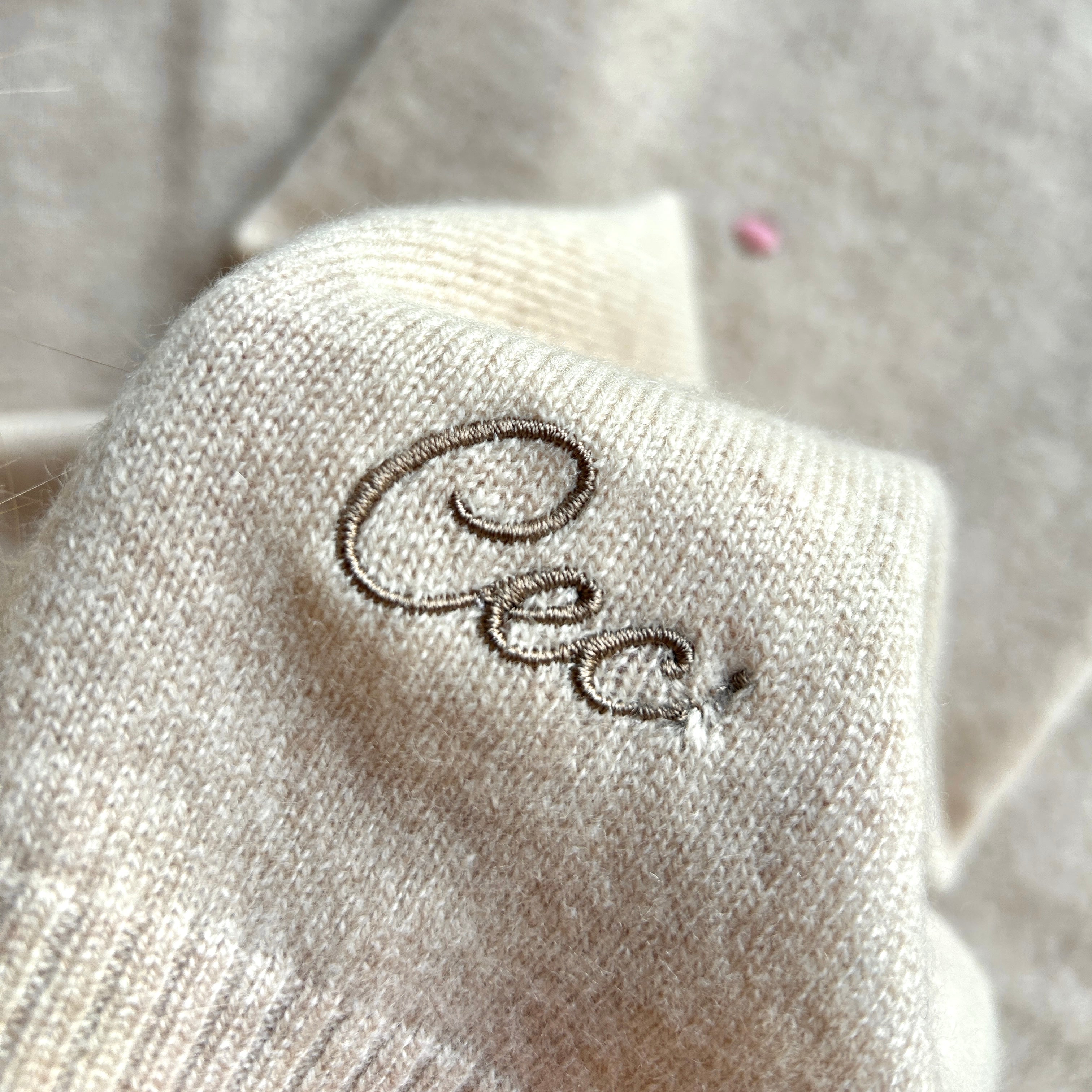 Detailaufnahme einer Kaschmirdecke in Beige mit Pinken Punkten. Bestickt mit Name "Cec" in Braun, Stickerei hat einen Stickfehler am Ende