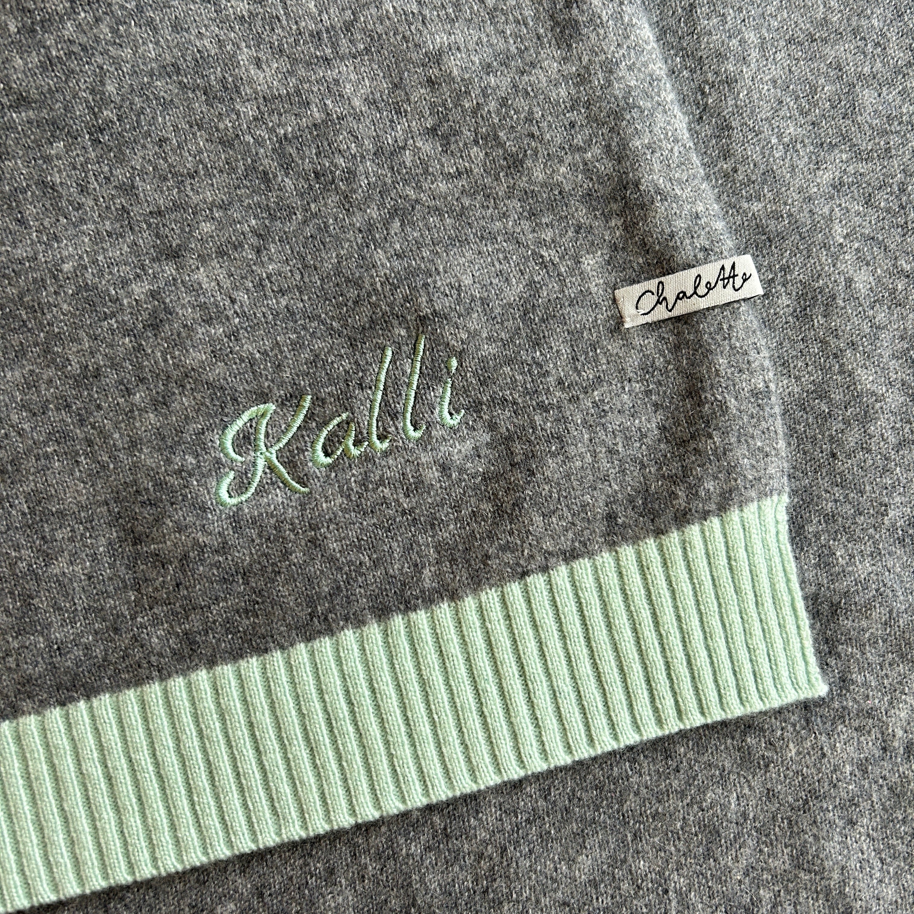 Kaschmirdecke in Grau mit Türkisfarbenen Rand. Bestickt mit Namen "Kalli" in Türkis